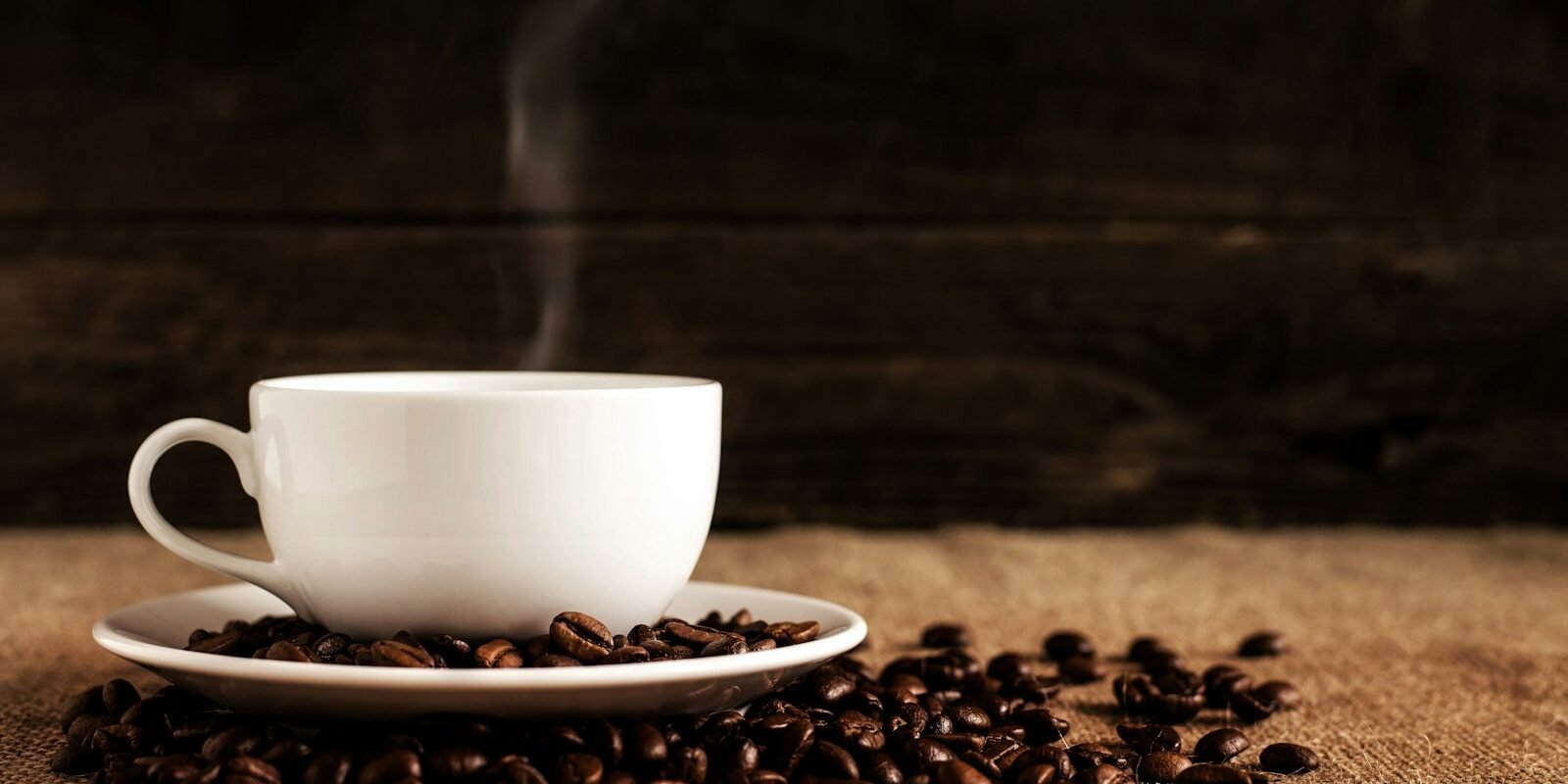 Café descafeinado y memoria: lo que vio un estudio con 62 adultos Taza blanca de café sobre un plato con granos de café tostado encima de una tela marrón
