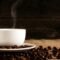 Taza blanca de café sobre un plato con granos de café tostado encima de una tela marrón