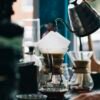 Persona vertiendo agua caliente en una cafetera de filtro de vidrio para preparar café