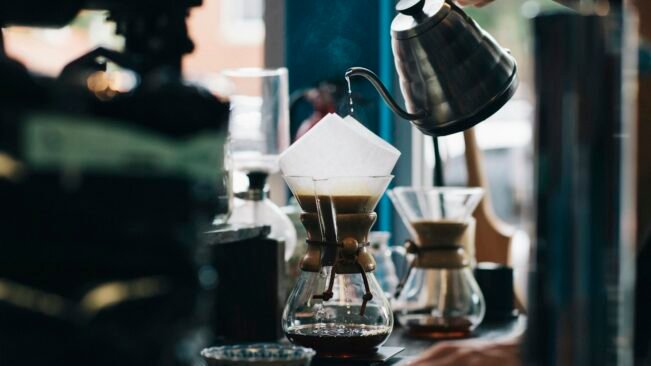 Café de filtro o soluble: qué vio un estudio sobre envejecimiento Persona vertiendo agua caliente en una cafetera de filtro de vidrio para preparar café