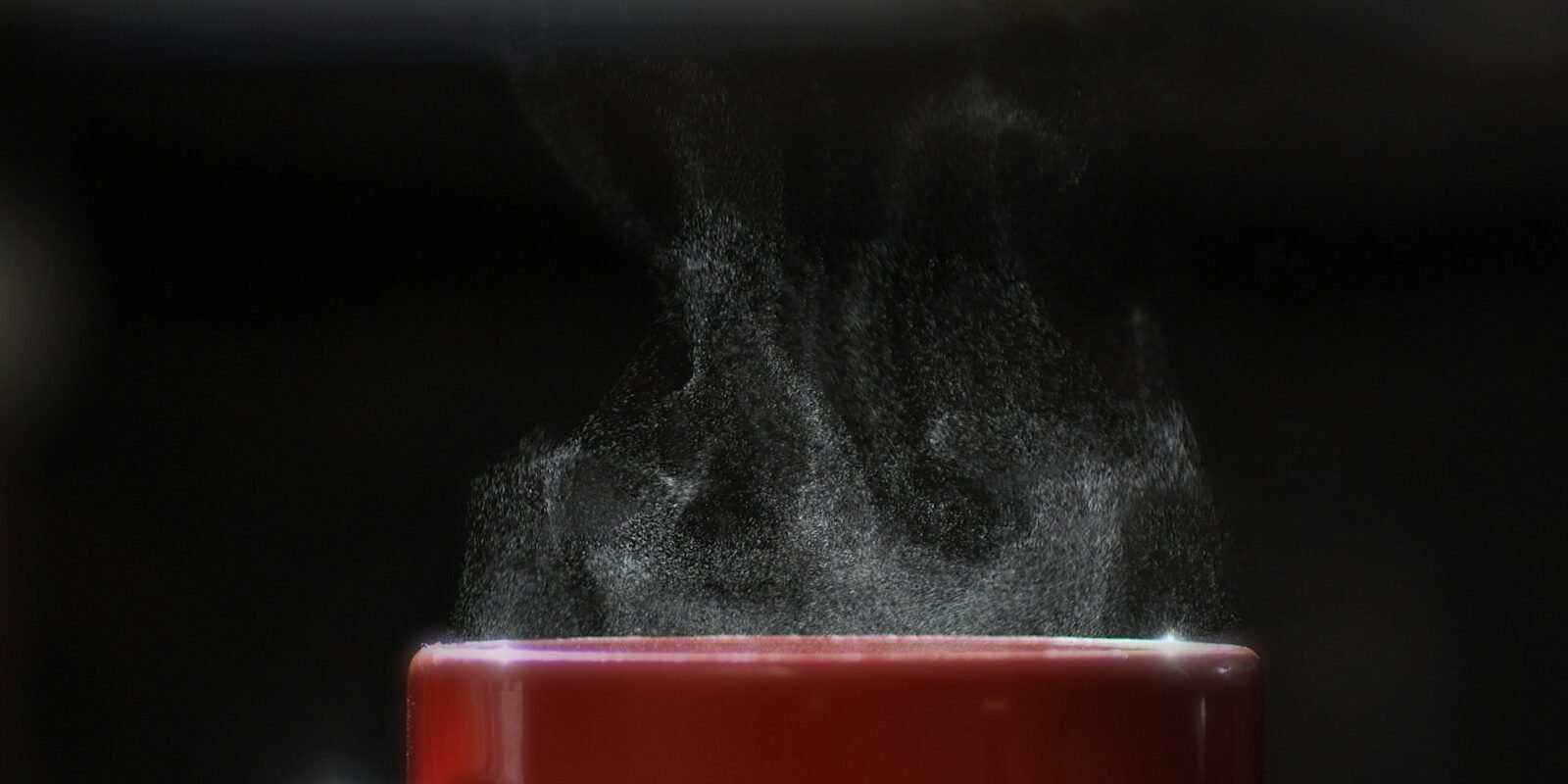 Taza de café humeante recién servida sobre una mesa, con vapor saliendo de la bebida caliente