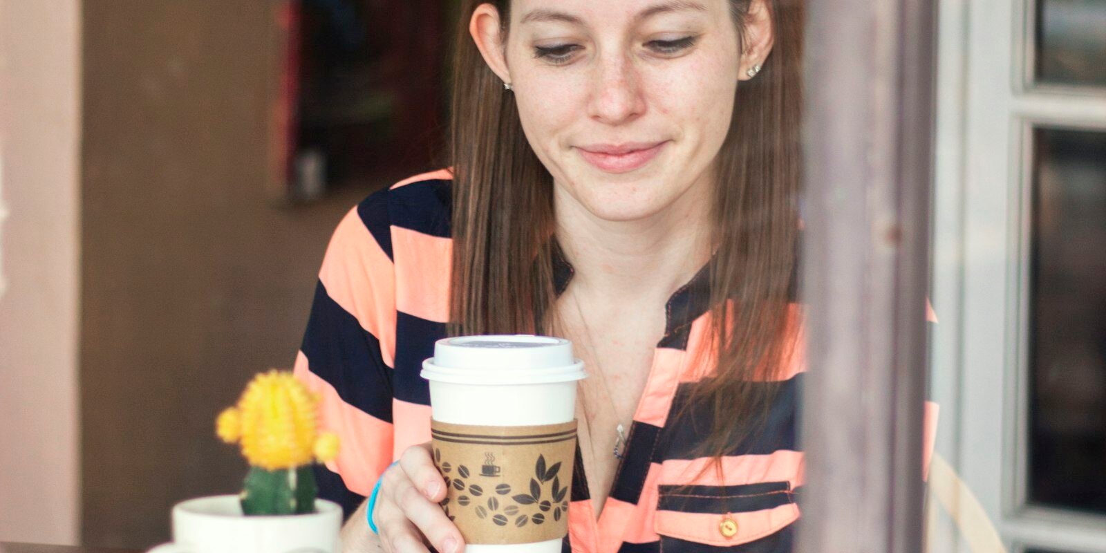 Café y migraña: qué dice una revisión de 19 estudios sobre la cafeína Mujer sentada a una mesa mirando la taza de café que sostiene en la mano