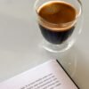 Taza de espresso junto a un libro abierto sobre una mesa blanca