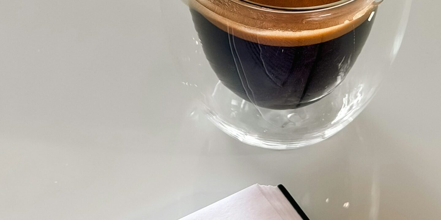 Taza de espresso junto a un libro abierto sobre una mesa blanca
