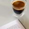 Taza de espresso junto a un libro abierto sobre una mesa blanca