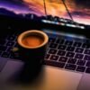 Taza de café negra sobre un portátil en un ambiente oscuro de noche
