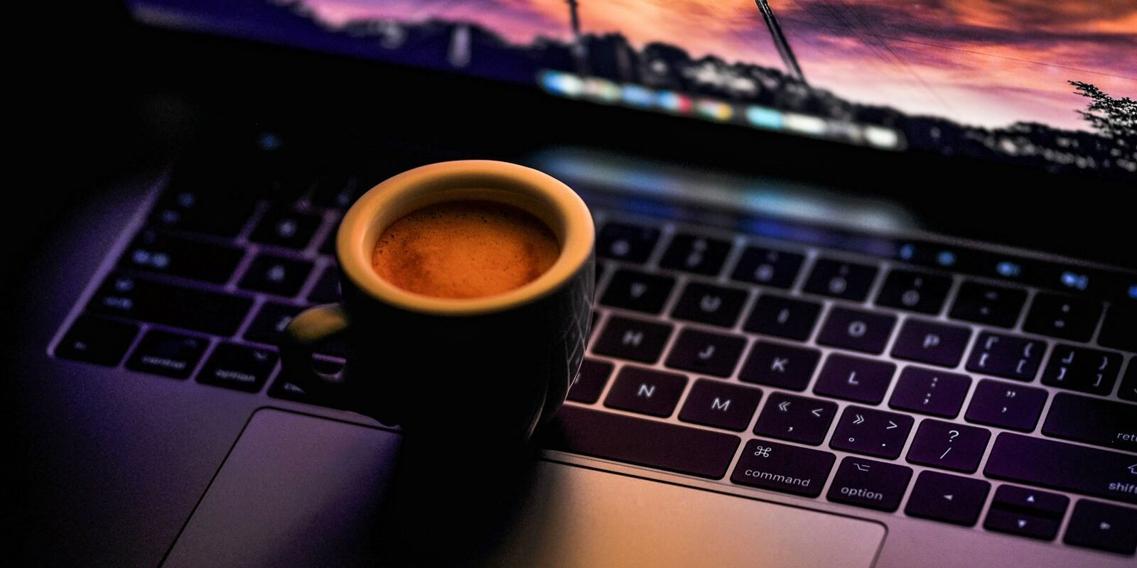 Taza de café negra sobre un portátil en un ambiente oscuro de noche