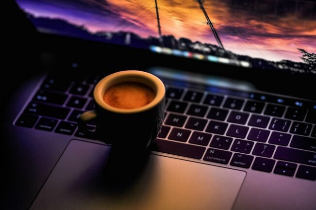 Taza de café negra sobre un portátil en un ambiente oscuro de noche