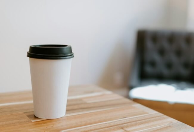 Vaso de café desechable de papel blanco sobre una mesa de madera