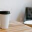 Vaso de café desechable de papel blanco sobre una mesa de madera